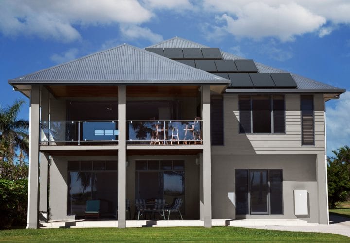 A modern house equipped with rooftop solar panels and a Tesla Powerwall energy storage system, showcasing a seamless off-grid solar power solution