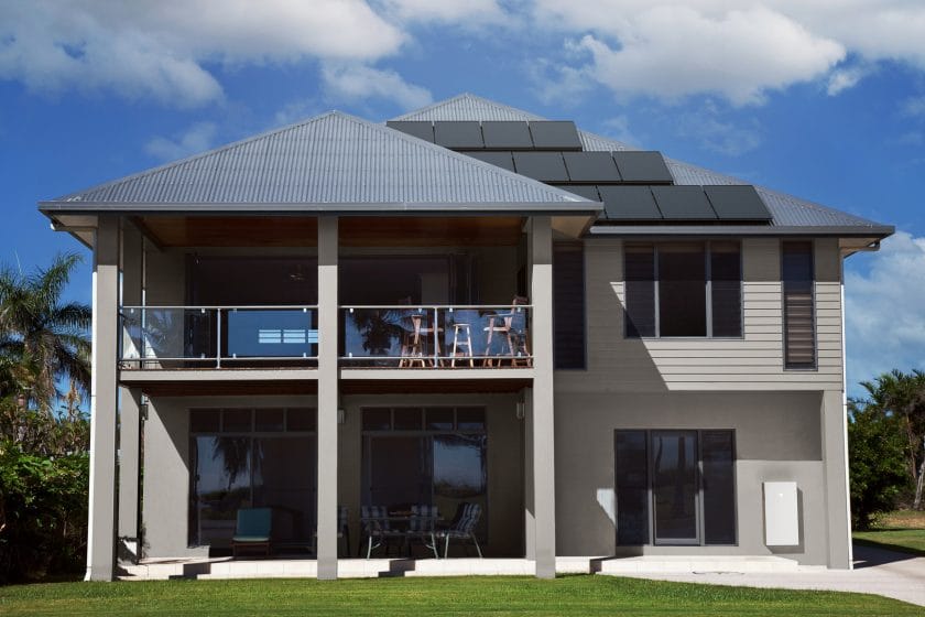 A modern house equipped with rooftop solar panels and a Tesla Powerwall energy storage system, showcasing a seamless off-grid solar power solution